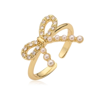 Gold-plated bow ring with cubic zirconia and pearls on a white background with reflection