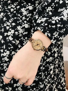 Detailed close-up of a vintage round gold quartz watch with a brown leather strap on wrist