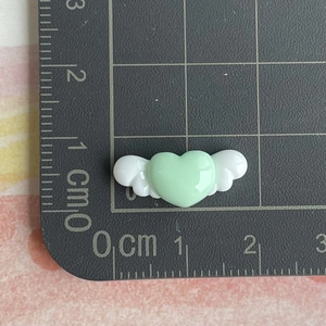 Detailed size view of a small mint green resin heart with white angel wings on a scale