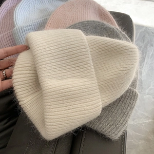 Close-up of thick knitted beanies in various pastel colors with soft faux fur texture