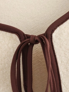 Dettaglio del tessuto sherpa color crema con bordi in tessuto marrone e laccio