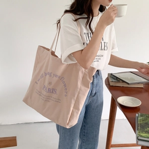 Detail of light pink canvas tote bag with purple Paris embroidery worn by a model