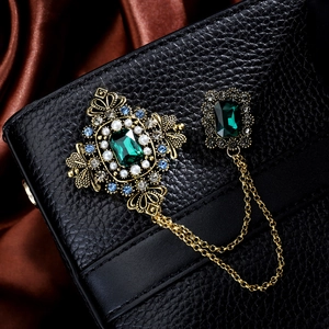 Detail of vintage gold chain brooch with green center stone and pearls on black leather