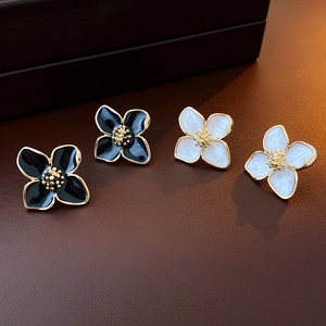 Détail des boucles d'oreilles fleurs en émail avec bordure dorée sur cuir sombre