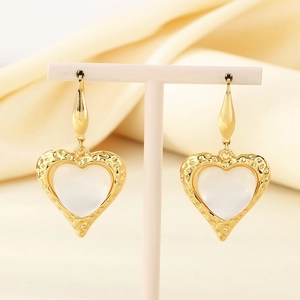 Macro view of gold heart earrings with hammered texture and white cat eye stone inlays