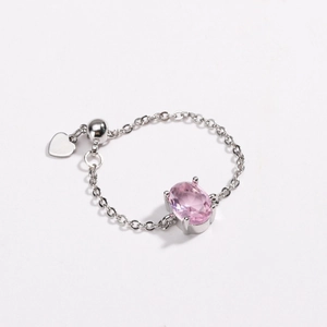 Detail of pink oval zircon ring with silver chain and a small heart pendant charm