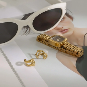 Detail of luxury gold square watch and twisted metal rings on a fashion magazine