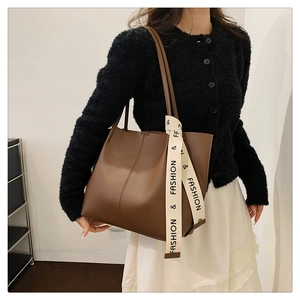 Detail of deep brown faux leather tote bag with a decorative ribbon on a model