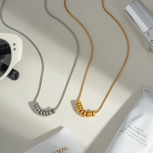 Detail of gold and silver snake chain necklaces with circular charms on a beige surface