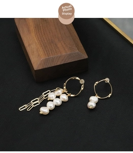 Detail view of asymmetric natural pearl earrings with gold tassels on a wood background