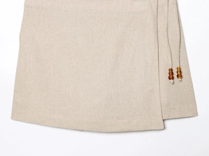Detail of beige cotton linen vest with adjustable drawstring and dark wooden beads