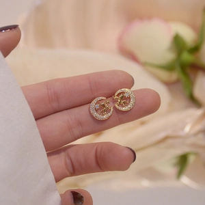 Macro shot of gold unicorn moon earrings with zircons on fingertip for size scale
