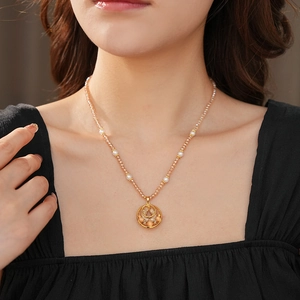 Close-up of a pearl beaded necklace with a golden openwork disc pendant on a neck model