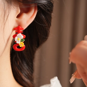 Macro shot of red Xi character earrings with delicate floral details and green leaves