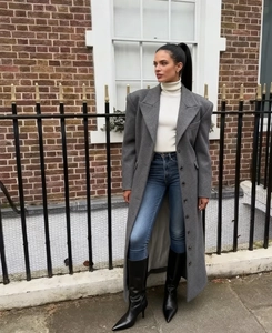 Dettaglio cappotto lungo di lana grigio scuro con dolcevita bianco e jeans blu attillati