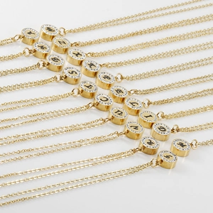 Détail de pendentifs ronds en acier titane doré 18K avec lettres et bordure en cristal