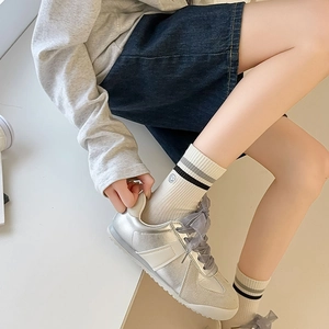Detail of grey crew socks with stripes paired with silver metallic sneakers and ribbon laces