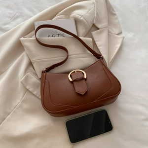 Detail view of brown lychee grain shoulder bag with golden hardware on a blazer background