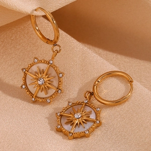 Détail de boucles d'oreilles boussole plaqué or 18K avec étoile et strass blancs