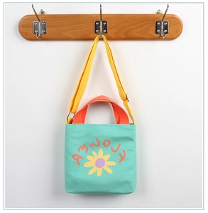 Close-up of green canvas kids bag with yellow daisy print and orange handles