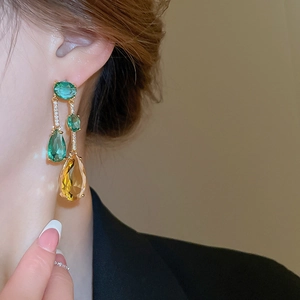 Détail de boucles d'oreilles pendantes avec zircons verts et jaunes sur un mannequin
