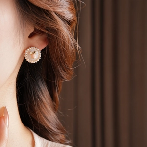 Detailed close-up of a floral pearl stud earring featuring pink enamel and a gold bow