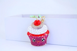 Detail of cute cupcake keychain with pink rhinestones and enamel cream on white background