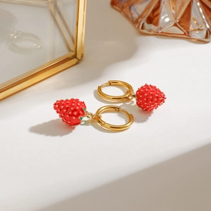 Cute red strawberry earrings with gold hoops and green leaf detail on a white surface