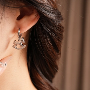 Close-up of silver metal hoop earring with a textured rocking horse pendant detail