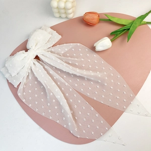 Detail of white swiss dot chiffon bow hair clip with long streamers on a pink display mat