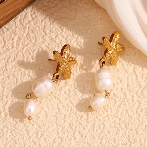 Macro shot of 18K gold starfish earrings featuring baroque pearls on silk background