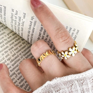 Detail view of a gold daisy enamel ring and a hollow butterfly ring on a hand