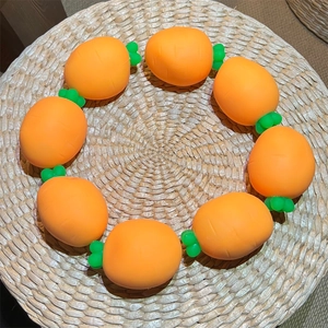 Detail of orange carrot-shaped beads on a silicone bracelet over a woven straw mat background