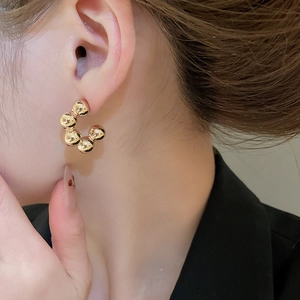 Detailed close-up of a model wearing a gold C-shaped earring made of six smooth spheres