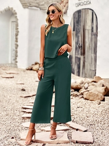 Deep green sleeveless top and wide-leg trousers set worn by a model in a sunny garden setting
