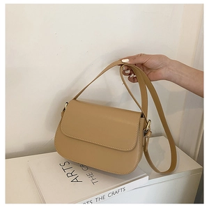 Detail of a khaki leather saddle bag hanging by its strap over a minimalist book