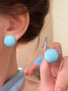Close-up detail of dopamine style bright light blue circular stud earrings on ear and hand