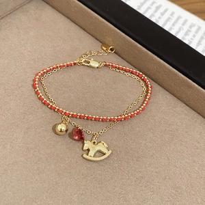 Close-up of a double-layer bracelet with golden horse charm, red gem, and woven cord