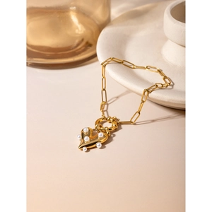 Detail of 18k gold heart pendant with pearls on a paperclip chain against a ceramic dish