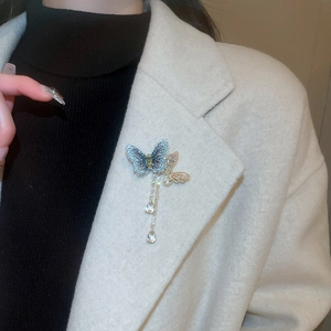 Detail of elegant butterfly brooch with blue embroidery and crystal tassels on white coat