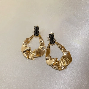 Detailed macro view of gold-tone pleated metal earrings with black gemstones and crystals