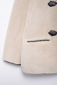 Détail du manteau en fausse fourrure crème avec texture douce et boucle en cuir marron foncé