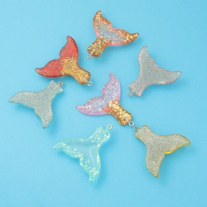 Macro shot of glittery resin mermaid tail charms with colorful gradient scales for jewelry