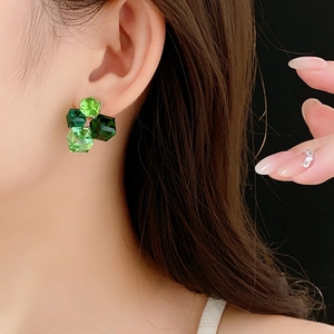 Detail shot of a woman wearing hexagonal green crystal stud earrings in a forest style