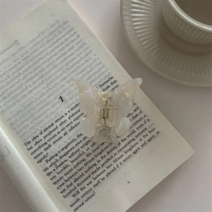 Close-up of white butterfly hair claw clip with pearlescent finish on vintage book pages