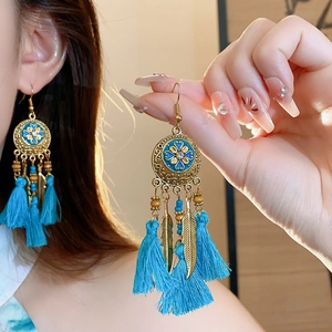 Nahaufnahme von Boho-Quastenohrringen mit blauen Emaille-Blumen und Federanhängern