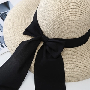 Primer plano de sombrero de paja beige con textura tejida fina y un gran lazo negro elegante