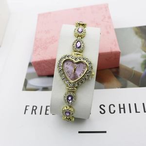 Détail de montre cœur dorée avec gemmes violettes et lunette sertie de cristaux