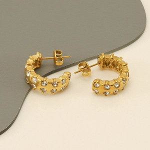 Detail view of gold-plated C-shaped earrings with clear zircon stones on a split background