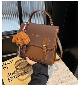 Detail of vintage brown leather handbag featuring golden metal buckle and plush charm accessory